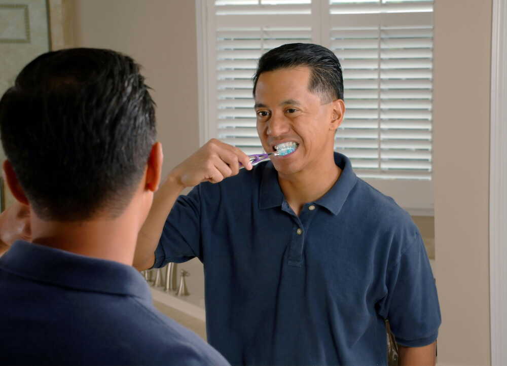 man brushing his teeth in mirror